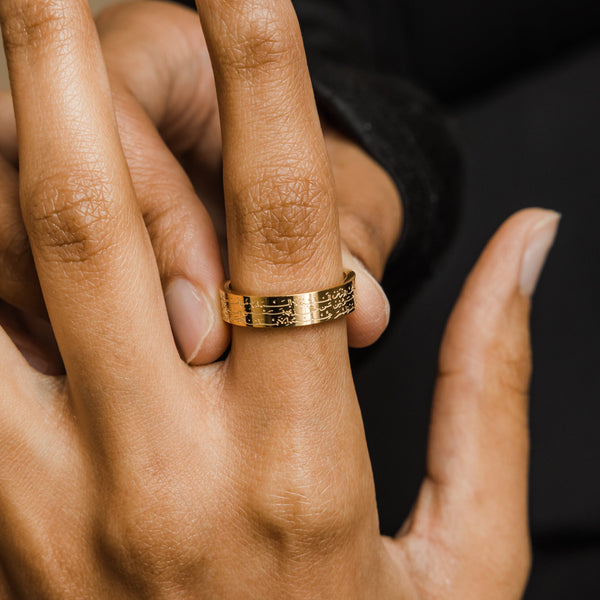 A close-up of a model's hand adorned with the 18K gold-plated Ayatul Kursi Ring. The ring's intricate Arabic script is prominently displayed, emphasizing the craftsmanship and design.