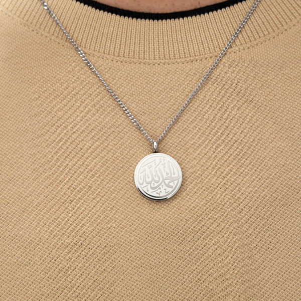 Silver Alhamdulillah token necklace worn on a beige textured shirt.