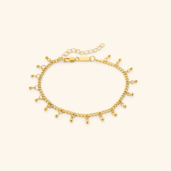A close-up of the Dangling Dotted Anklet in 18K gold plating. The anklet features a delicate curb chain with evenly spaced 3mm ball-shaped charms that dangle, creating a subtle and elegant design.
