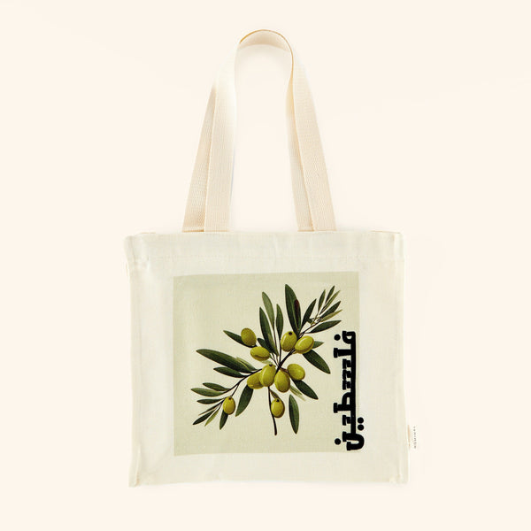 A textured cotton canvas tote bag featuring a vibrant olive branch print and the word "Palestine" elegantly scripted in Arabic. The tote measures 13 inches in height, 12 inches in width, and 3.5 inches in depth, with an 11-inch strap drop. It includes a zip closure and one open interior pocket.
