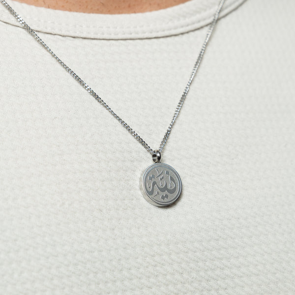 Silver Intention token necklace worn on a textured white top.