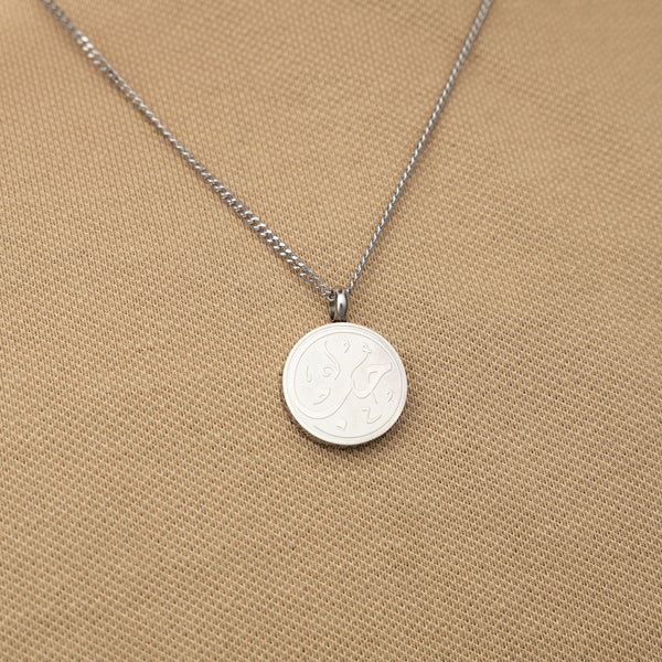 Silver love token necklace worn over a beige textured shirt.