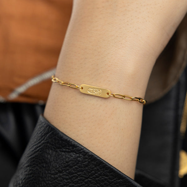 Close-up shot of gold Arabic-engraved My Sister Ukhti Link bracelet, styled over a black leather sleeve.