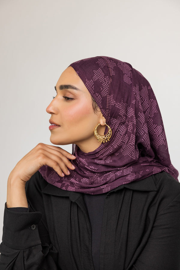 A female model with medium skin tone wearing the 18K gold-plated Jasmine Crescent Hoop Earrings. The earrings dangle elegantly from her ears, complementing her minimalist outfit and highlighting the intricate jasmine vine design