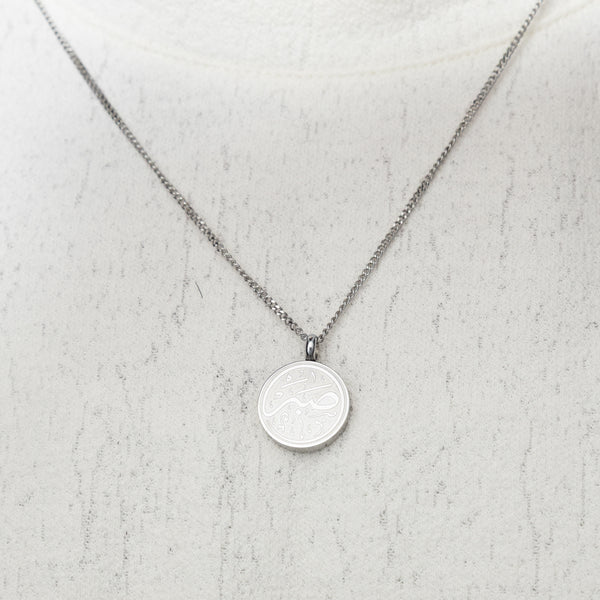 Silver Patience Token necklace worn on a white textured top.