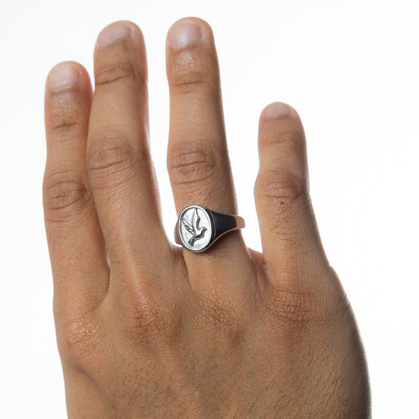 Hand raised, a silver ring of tranquility showing the engraved dove, worn on the ring finger.