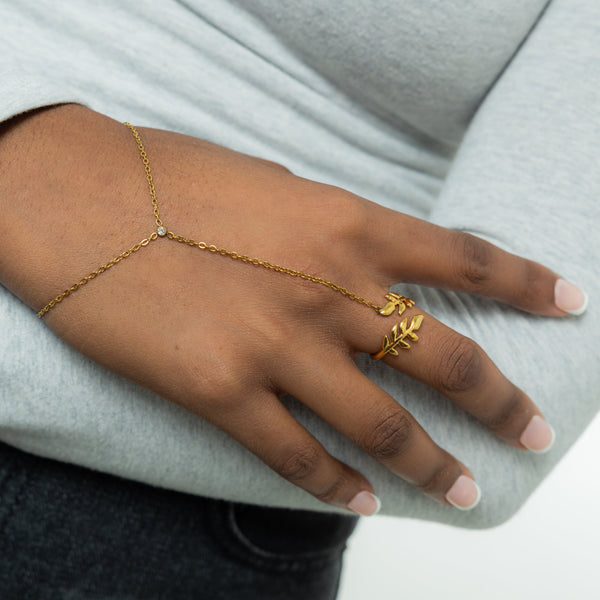 A model wearing the 18K gold-plated Shining Olive Hand Chain. The hand chain drapes elegantly from her finger to her wrist, highlighting the olive leaf design against her skin.