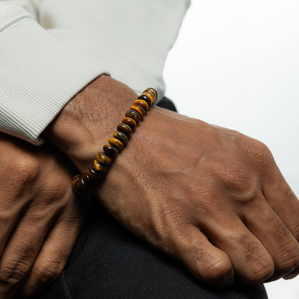 A man wearing the Soulful Bead Bracelet on his wrist. The bracelet is made of round Tiger’s Eye beads in brown and gold tones.