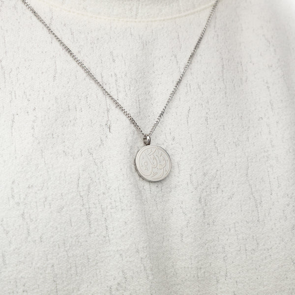 Silver trust token necklace worn on a textured white top.