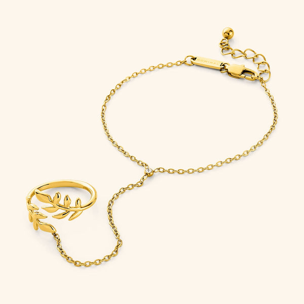 A close-up of the Shining Olive Hand Chain in 18K gold plating. The hand chain features a delicate chain connecting a ring adorned with an olive leaf design to a bracelet, symbolizing heritage and resilience.