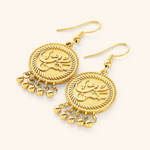 A pair of gold-plated vintage coin earrings displayed on a white background. Each earring features a round pendant engraved with the Arabic word "مكتوب" (Maktub), meaning "It is written," and is adorned with three small dangling orbs at the bottom.