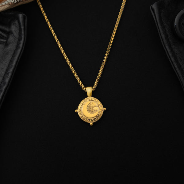 Gold necklace with a round pendant featuring the engraved phrase 'What you seek is seeking you' in Arabic calligraphy. The design includes a raised crescent moon and a flowing motif, framed with vine detailing and three small bead accents around the border. 