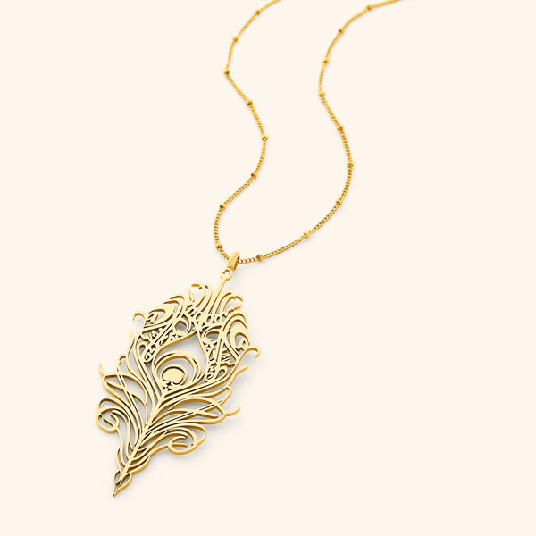 A delicate gold-plated chain necklace featuring a stylized, peacock feather-shaped pendant with intricate cut-out details. The pendant and chain are displayed against a light beige background.