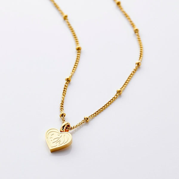 A close-up of the gold-plated "Sister Love" necklace by Nominal. The pendant features elegant Arabic calligraphy. The delicate chain is visible.