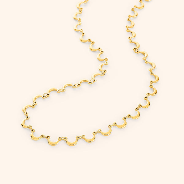 A close-up of the Skyfall Necklace in 18K gold plating. The necklace features a seamless chain of crescent-shaped charms, draping gracefully like a constellation in motion.