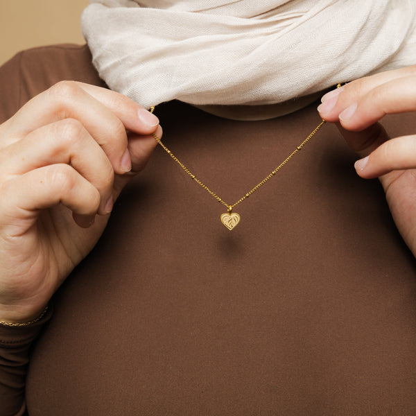 A person wearing the "Sister Love" necklace by Nominal. The gold pendant with Arabic script rests on their neck.