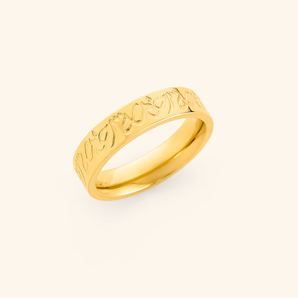 Gold band ring engraved with "Rahma" in Arabic calligraphy, displayed on a soft cream backdrop.