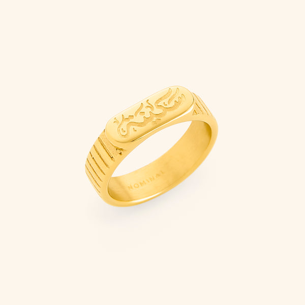 Gold ring with engraved “Sakinah” in Arabic calligraphy and lined side detailing. Inner of the band stamped with “NOMINAL.”