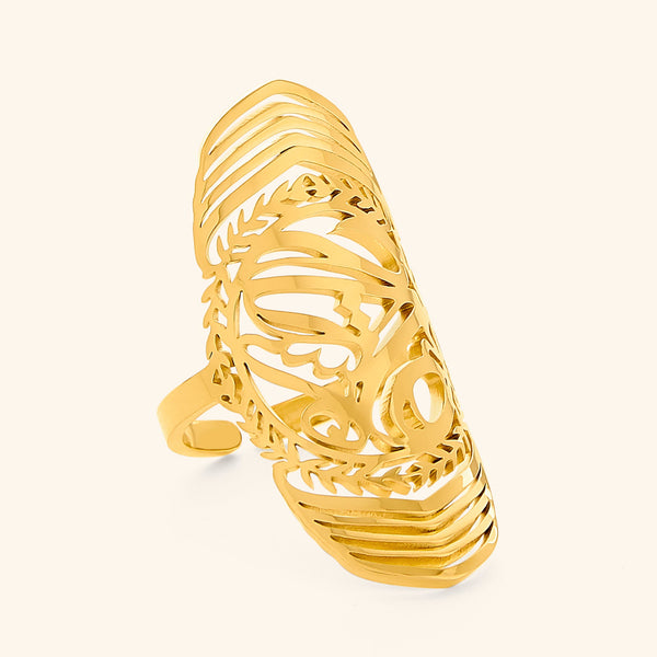 A gold ring with intricate cut-out designs, inspired by ancient artistry. The ring is long and features detailed patterns, possibly with floral or geometric motifs. The text "SUFFICIENT (ring) - Women | Aadil x Nominal" suggests this is a product shot for a women's ring, possibly a collaboration between Aadil and Nominal.