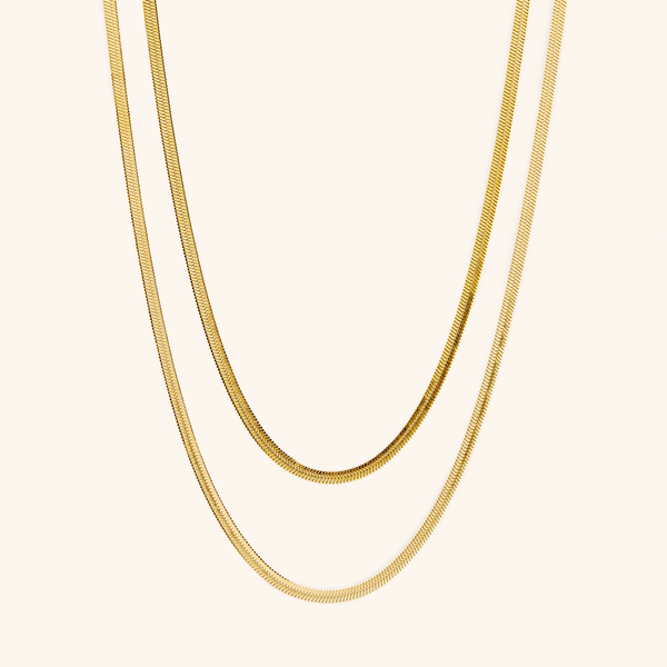 Two gold herringbone chains laid flat against a cream background.