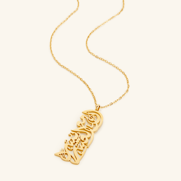 A close-up of the "With Hardship Comes Ease" Calligraphy Necklace in 18K gold plating. The necklace features a rectangular pendant engraved with the Arabic verse "إِنَّ مَعَ الْعُسْرِ يُسْرًا" ("Verily, with hardship comes ease") from the Qur'an, suspended from a delicate chain.